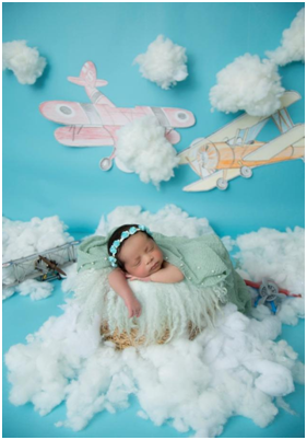 A newborn sleeping in a basket surrounded by creative props.